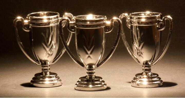 Three trophies in a row in front of a black back drop