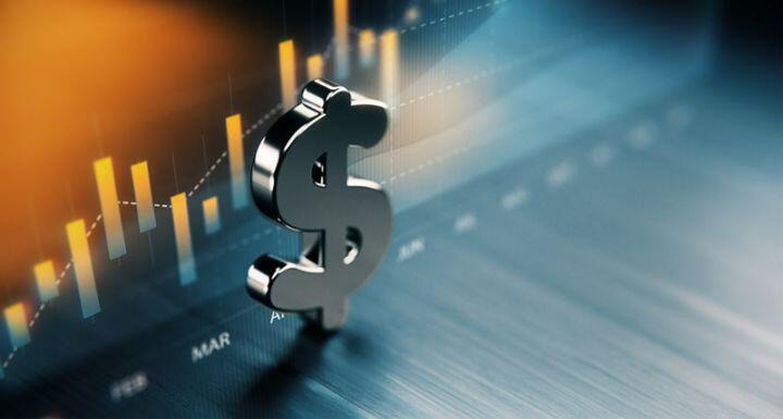 American dollar symbol standing on wood surface in front of a graph