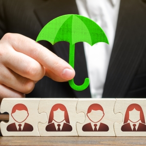 Business holding umbrella over employee icons on wooden puzzle pieces