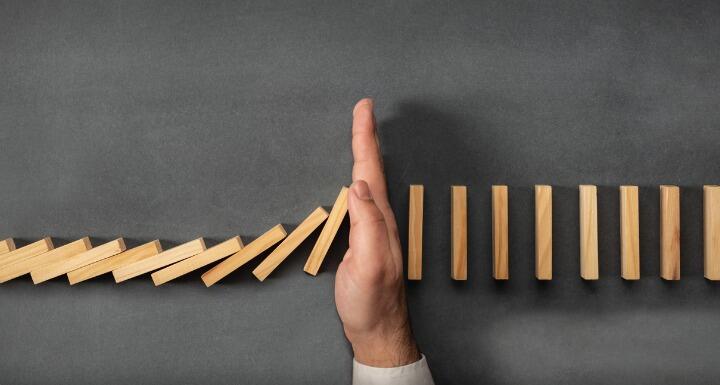 Businessman hand stopping falling dominoes