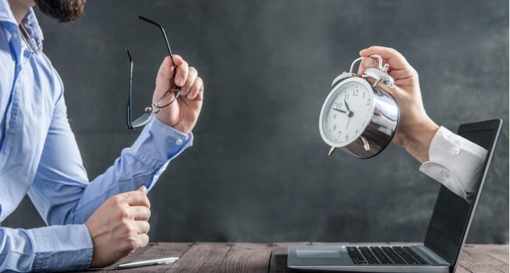 Businessman looking at laptop with clock coming out with clock