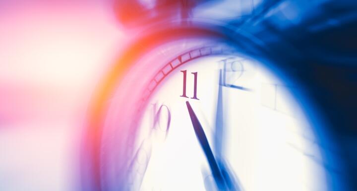Blurred clock with the hands showing eleven o'clock