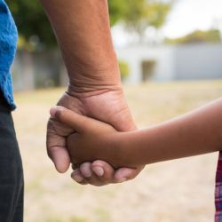 A close up image of a grandparent holding the hand of a child