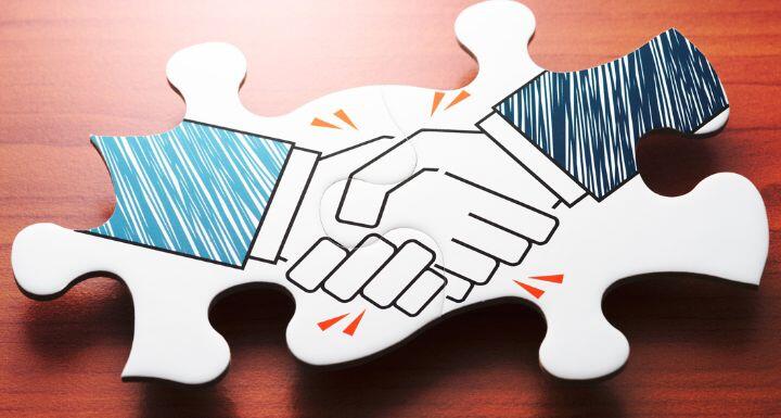 Handshake jigsaw puzzle pieces on wood desk