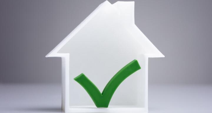 Small white house on a tabletop with a green check mark on the house