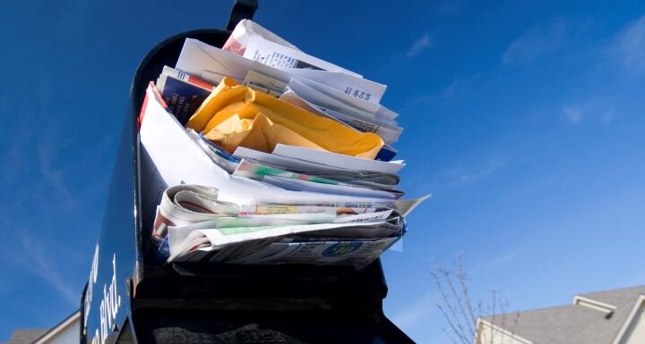 An open black residential mailbox completely overstuffed with mail